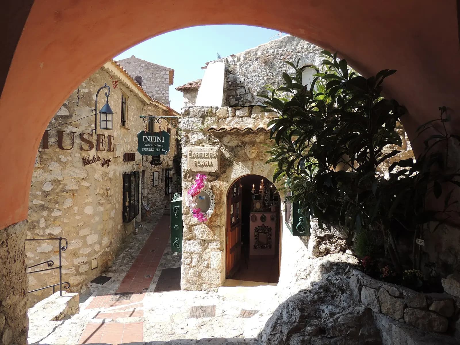Ruelle pavée d'Èze vue sous une arcade, entre maisons de pierre et boutiques