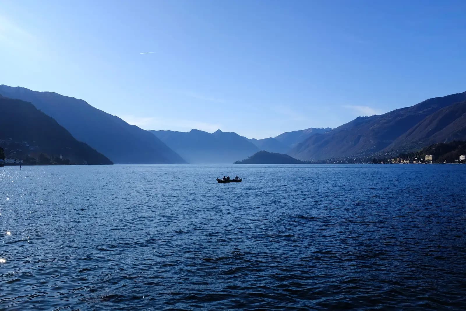 Der Comer See von Bellagio aus gesehen, ein kleines Boot auf dem Wasser zwischen bläulichen Bergen