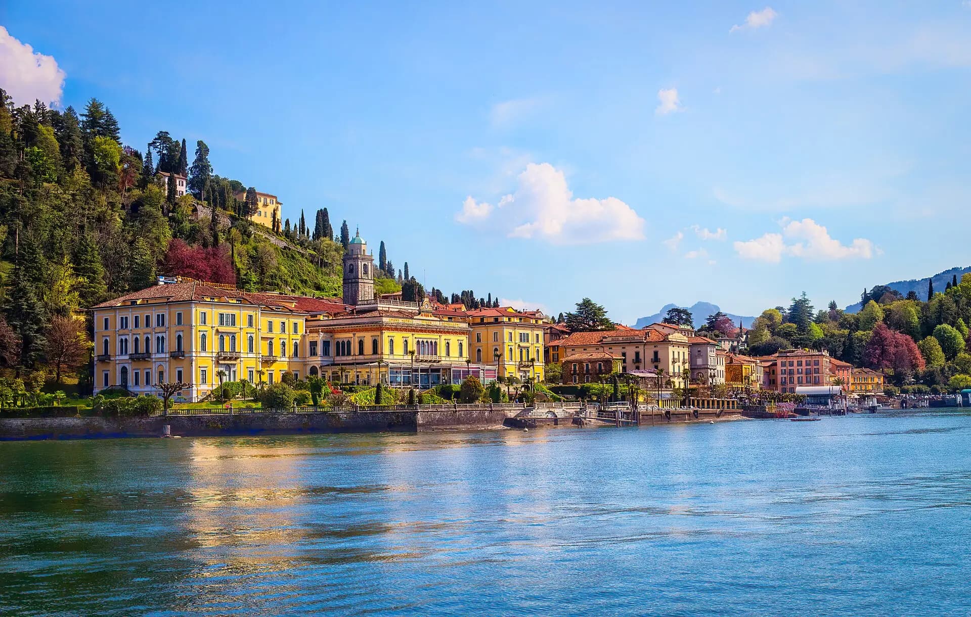 Die Uferpromenade von Bellagio mit gelben und ockerfarbenen Fassaden am Comer See unter blauem Himmel