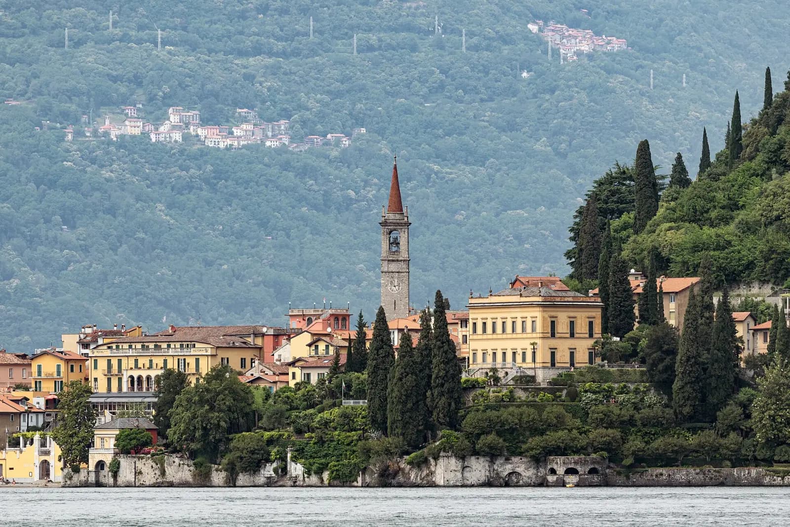 Glockenturm und Häuser von Varenna am Seeufer, umgeben von Zypressen