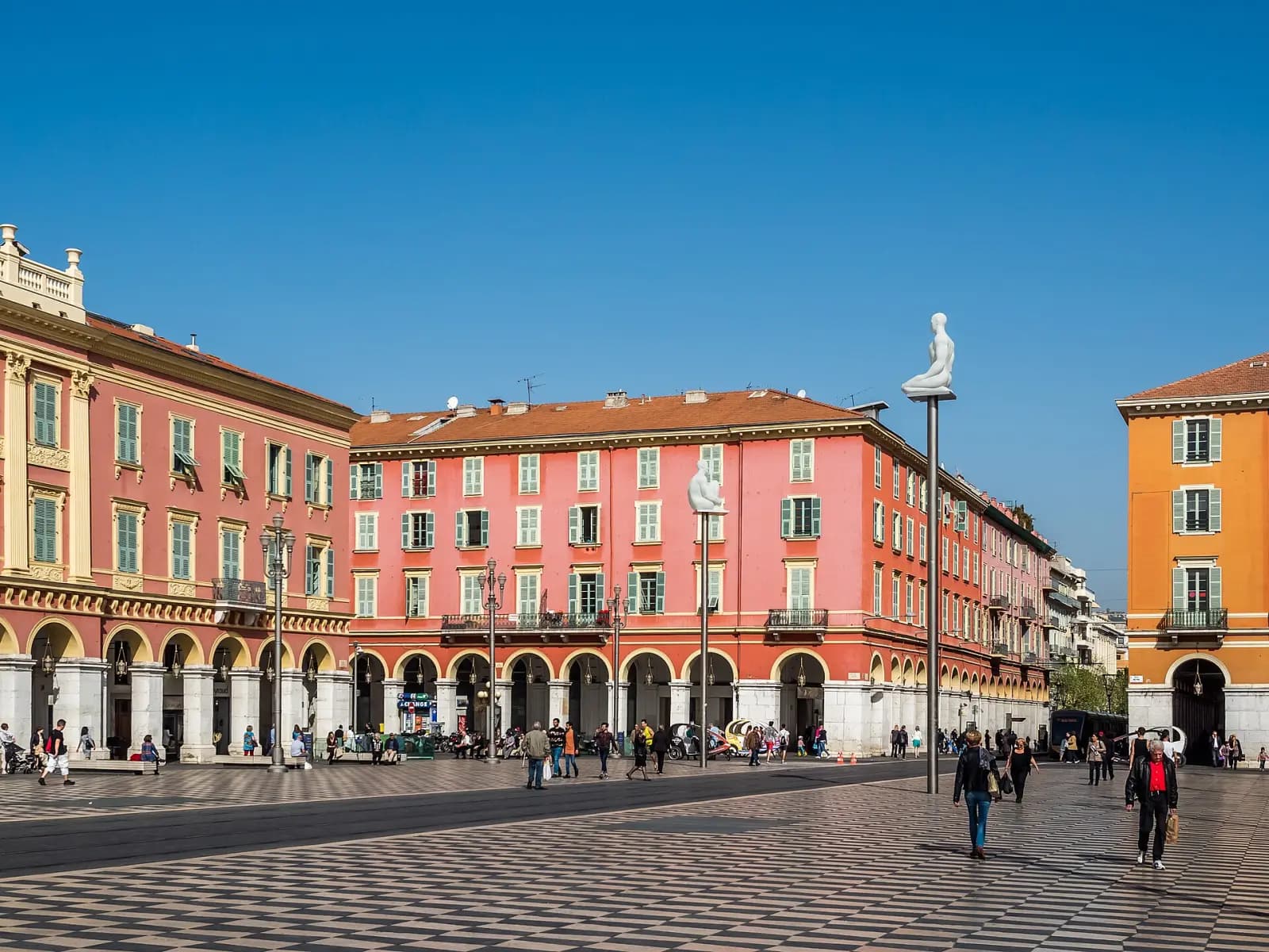 Red arcaded buildings and chequerboard paving on Place Masséna under a blue sky