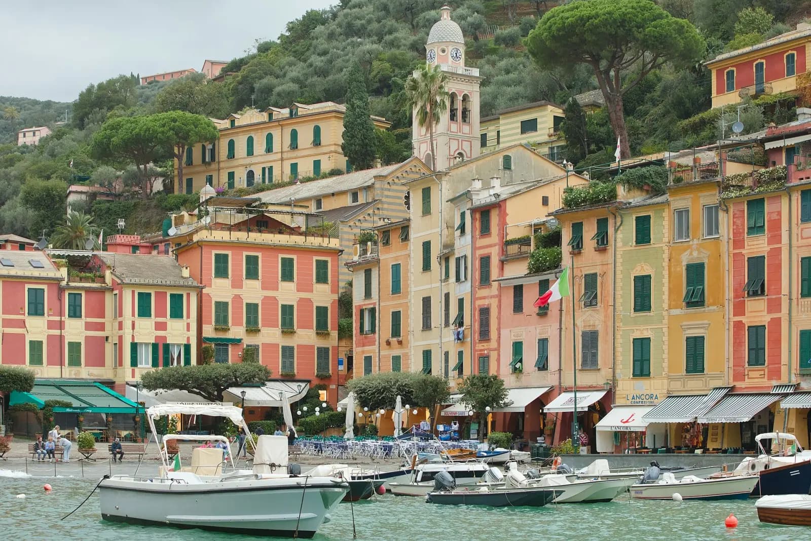 Bunte Fassaden und ein Glockenturm über dem Hafen von Portofino, davor Boote an der Piazzetta
