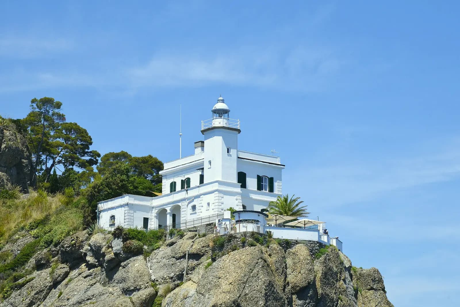 Der weiße Leuchtturm der Punta Portofino auf seinem Felsen unter blauem Himmel