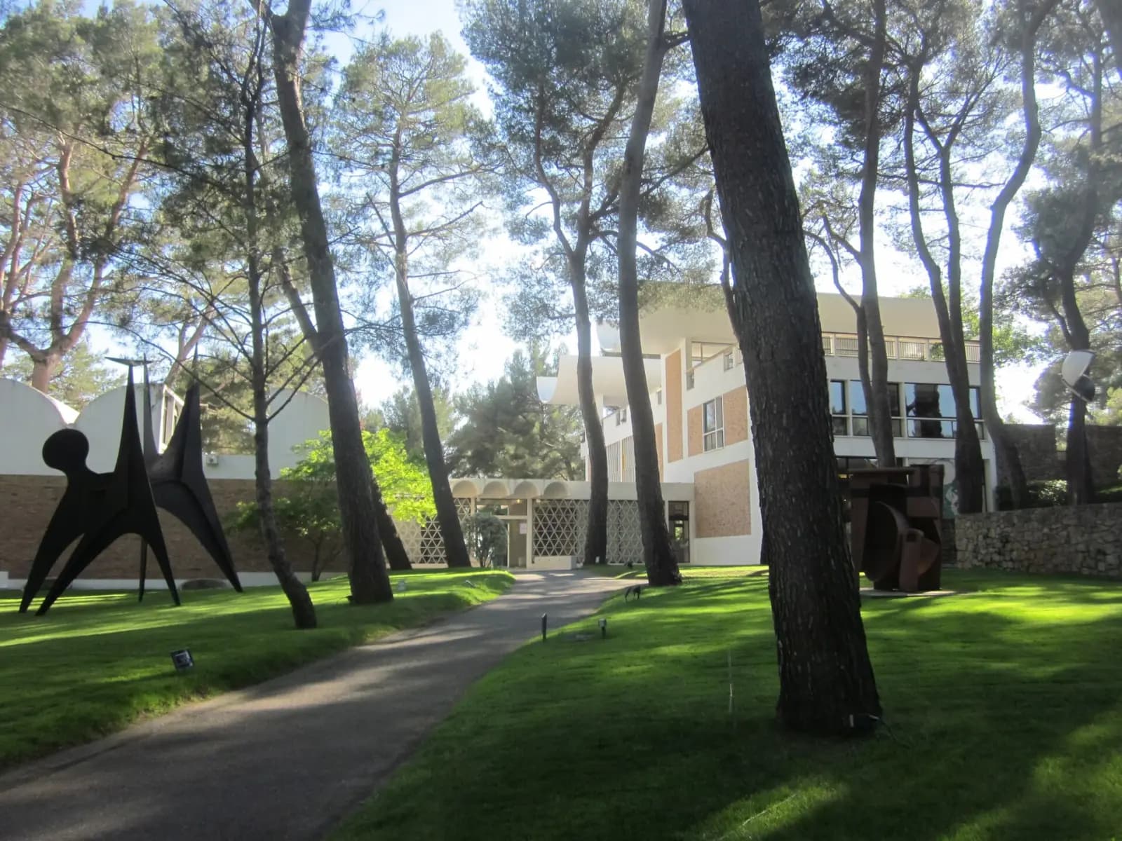 Sculpture noire sur la pelouse ombragée de pins de la Fondation Maeght