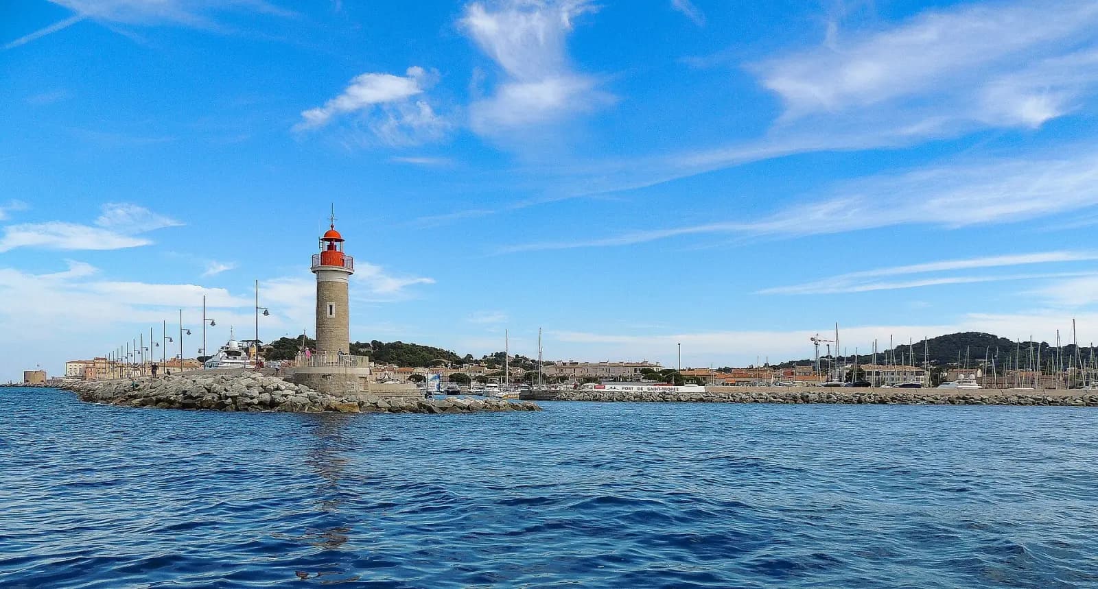 Le phare rouge au bout de la jetée du port de Saint-Tropez, la mer et les collines du golfe